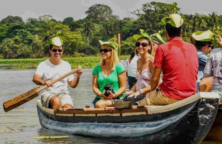 A group of visitors wearing woven leaf hats, rowing a wooden boat on the lake