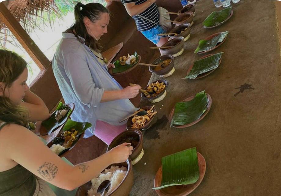 Visitors serving themselves village-cooked curries from clay pots onto banana leaves