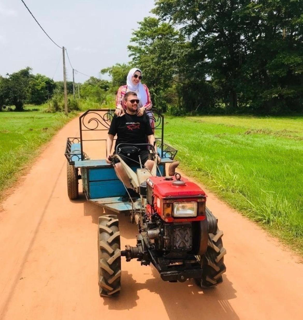 Visitors standing on a trailer towed by a farm tractor on a village road